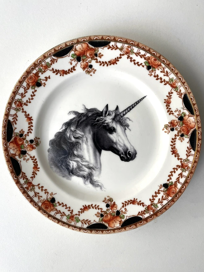 vintage plate with an ornate border, with a printed vintage illustration of a unicorn in the middle 