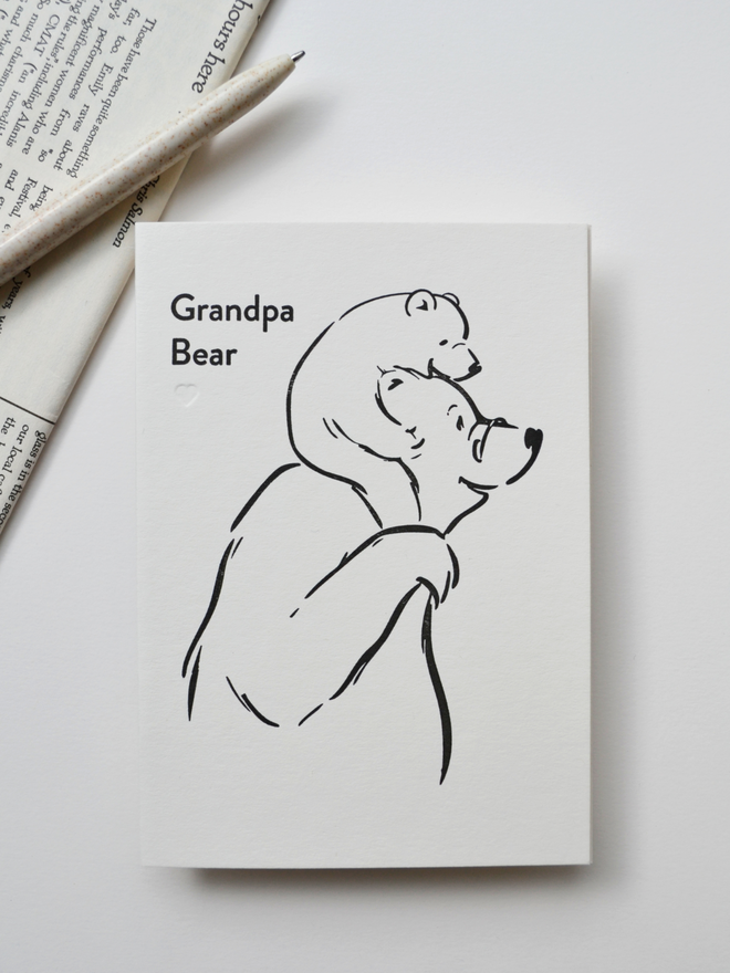 greeting card for Grandpa with simple bear character illustration.  Black and cream with newspaper and pen in background