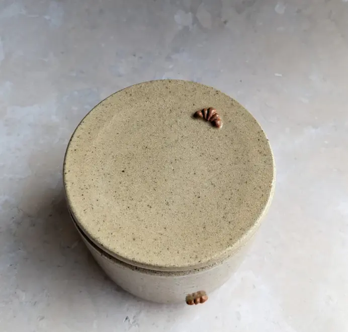 Croissant Butter Crock in biscuit glaze with a small croissant design on the front, set against a grey background.