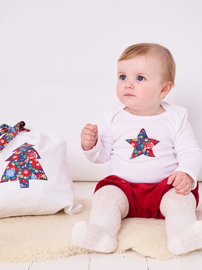 A baby wearing a christmas star white bodysuit featuring a star on the front in liberty fabric