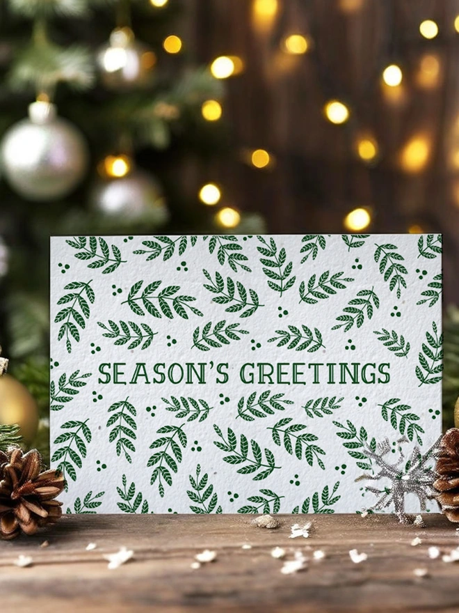 Christmas card with 'Seasons Greetings' on it surrounded by green leaves. The card is in a Christmas scene