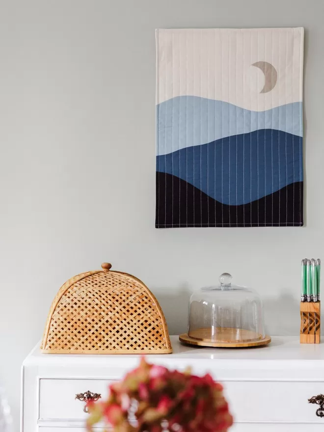 Crescent Quilt Hanging On Wall Above White Cupboard