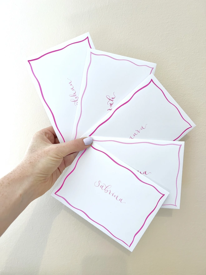 Four white envelopes with pink wavy borders and pink handwritten names inside the border