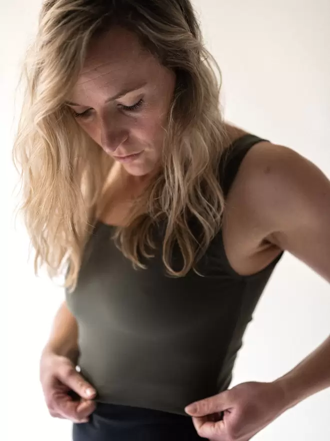 A close up of a blonde lady looking down and holding the material of the Davy J Sustainable Swimwear olive cropped swim top that she is wearing. The lady also wears a pair of black high waisted bikini briefs