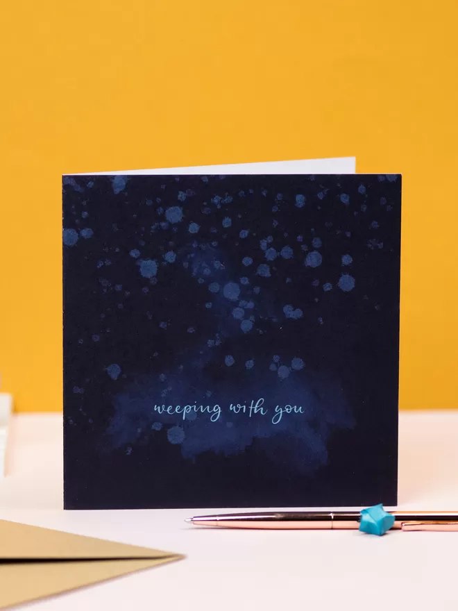 'Weeping With You' Grief Card seen with a yellow wall behind.