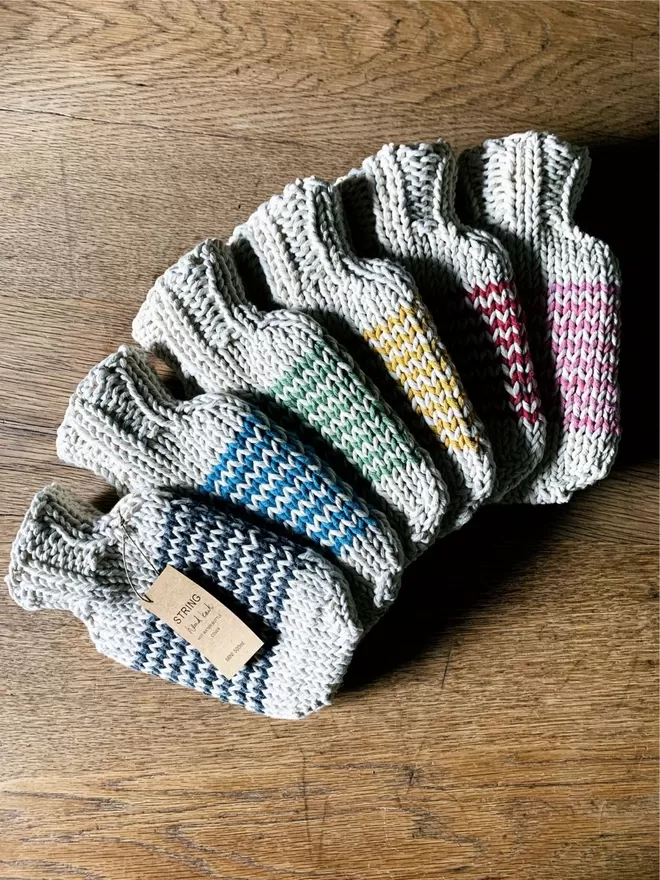 Six hand knitted String Mini Hot Water Bottles with contrast colour stripes on an oak table