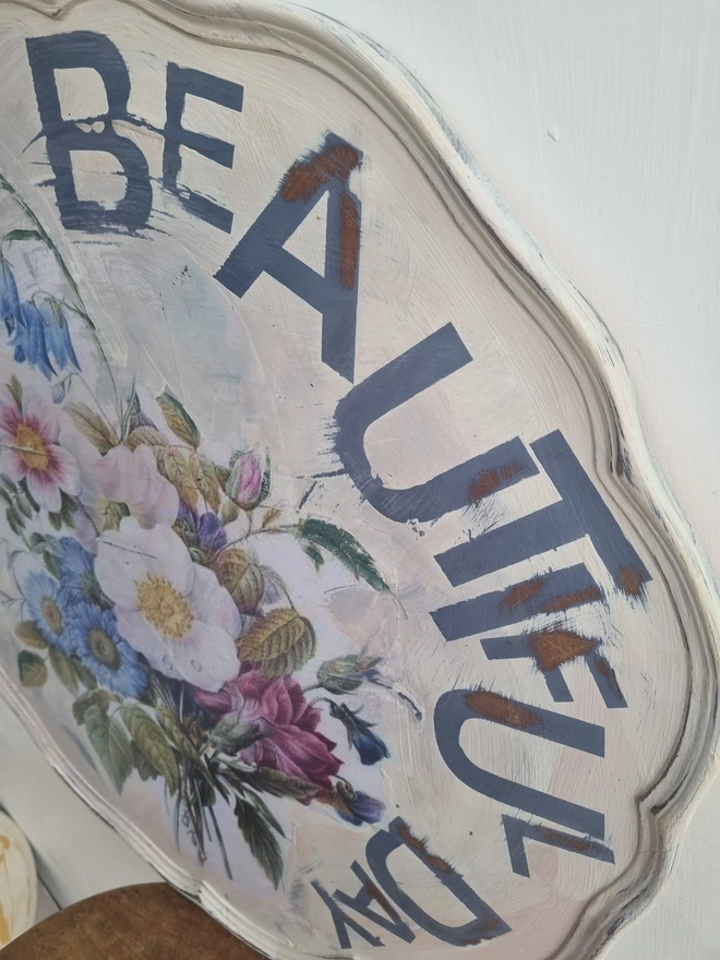 Art Panel made from a 'pie crust' table top. A pale background with mauve flowers and writing in mauve that says 'what a beautiful day'.