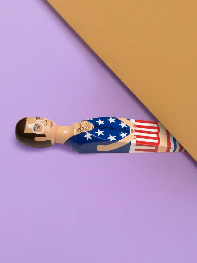 Wooden Door Stopper (Elty Stars & Stripes Outfit), a colourful wooden door stop sitting under a door.