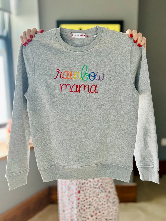 Lisa Macario holding a grey sweatshirt embroidered with the words rainbow mama