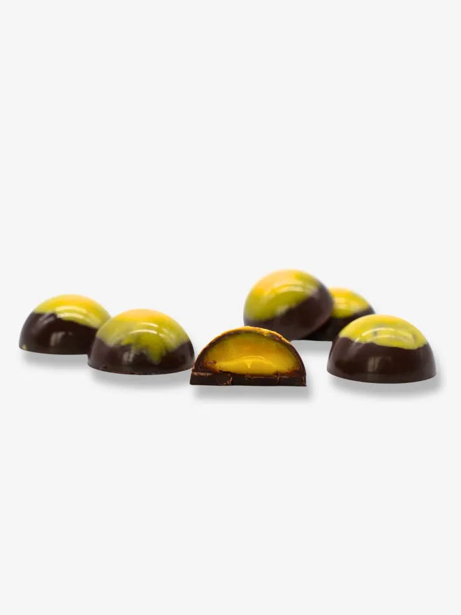 six luxury dark chocolates with one cut in half revealing a mango and calamansi filling