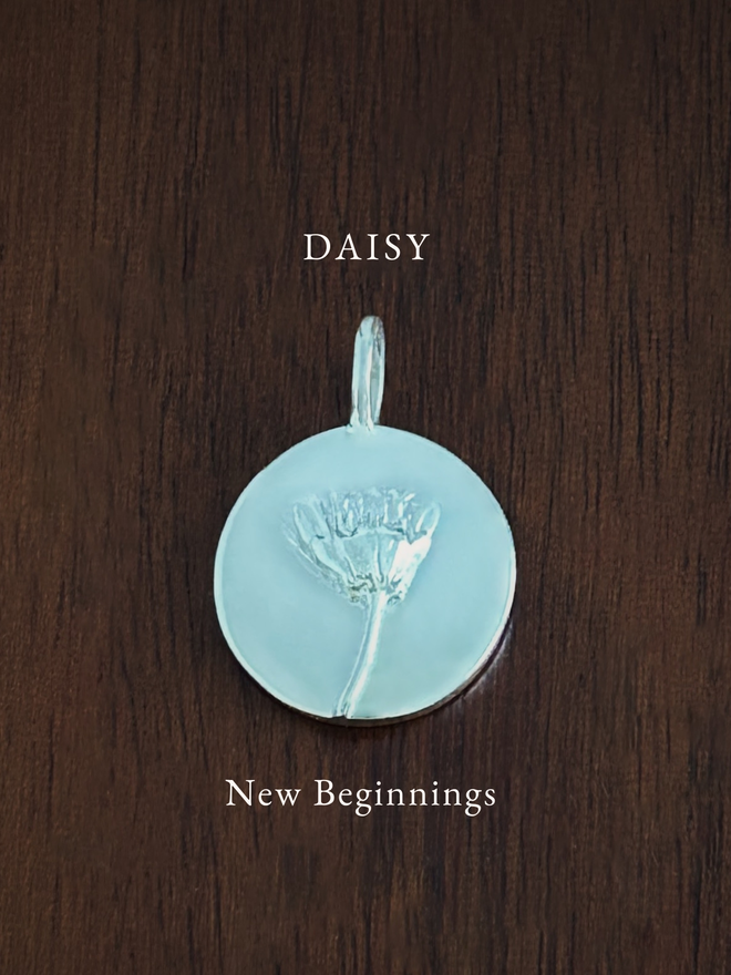 Sterling Silver Daisy Coin Charm on a dark background with the language of flowers meaning, new beginnings