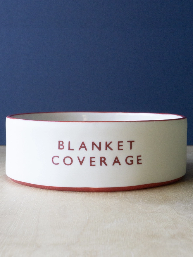 Ceramic porcelain dish with Blanket Covering written on the side. A white Christmas serving dish with red rim. 