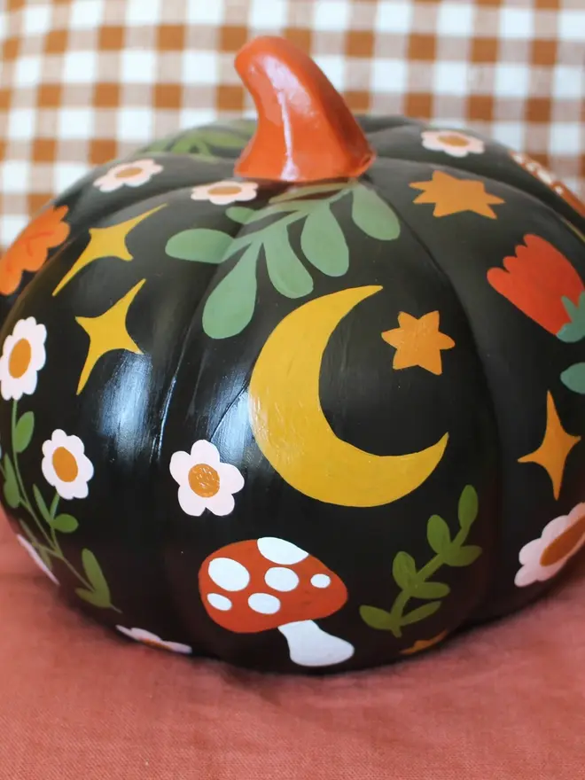 hand-painted folk art ceramic pumpkin. a black ceramic pumpkin painted with mushrooms and flowers.
