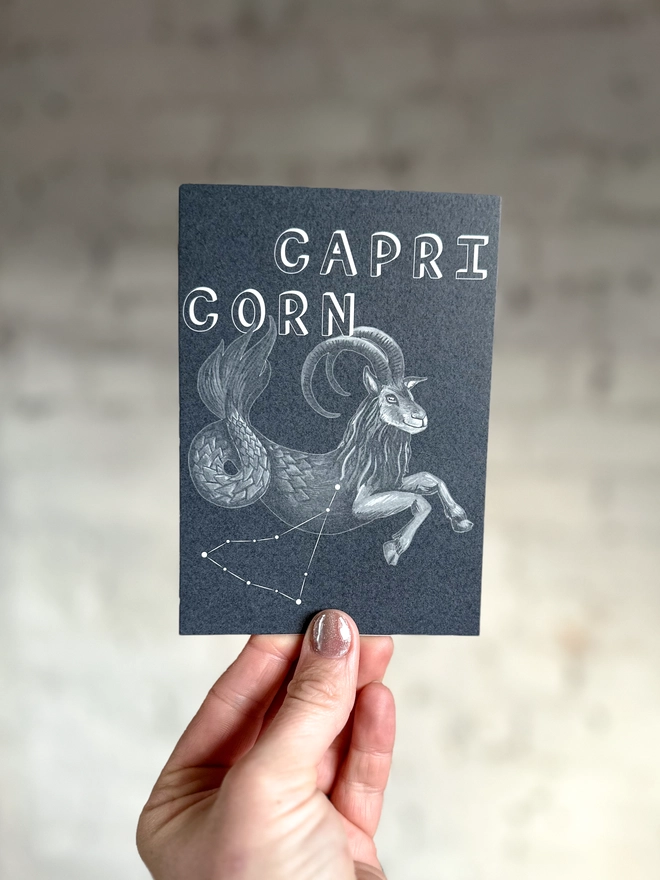 a greetings card featuring a greyscale illustration of a zodiac style sea goat with the text “CAPRICORN”