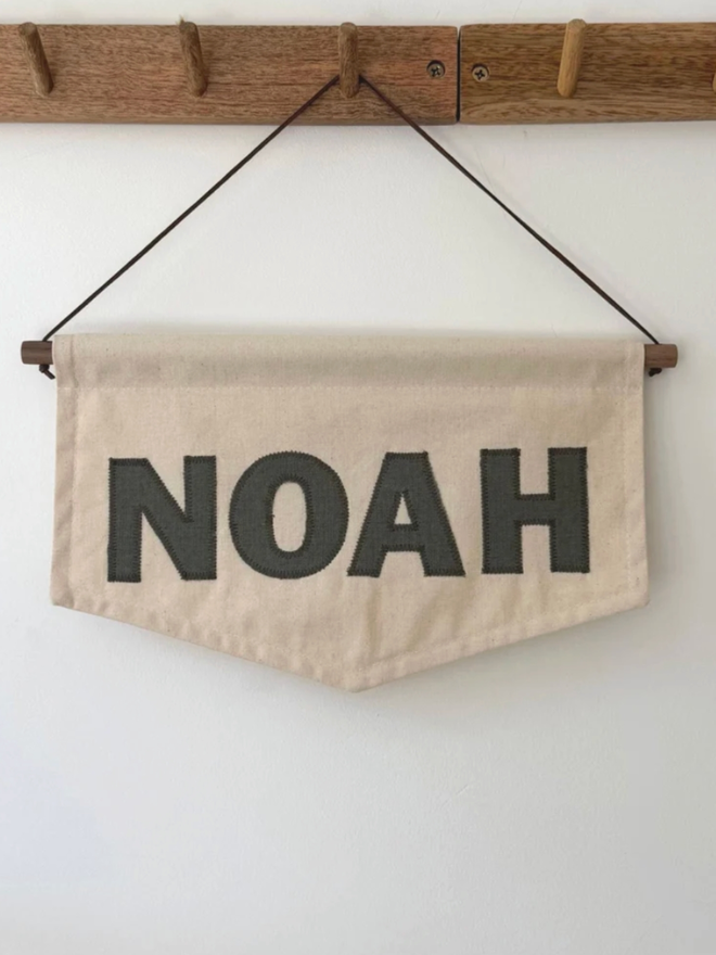 Linen Personalised Banner. A banner in small with ‘NOAH’ hung on a wall.