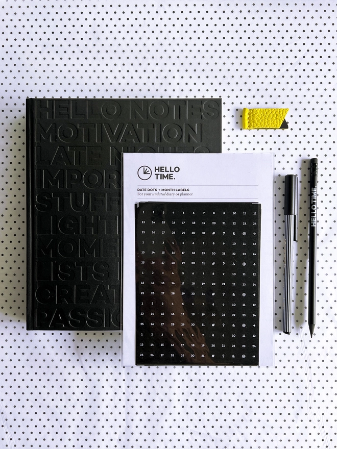 HELLO TIME Life Planning Kit flatlay with black notebook, date stickers, yellow leather page marker, pencil and fineliner