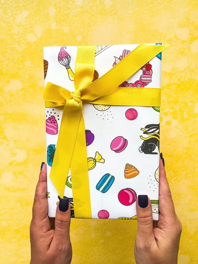 a person holding up a gift wrapped in colourful macaron paper and a yellow ribbon