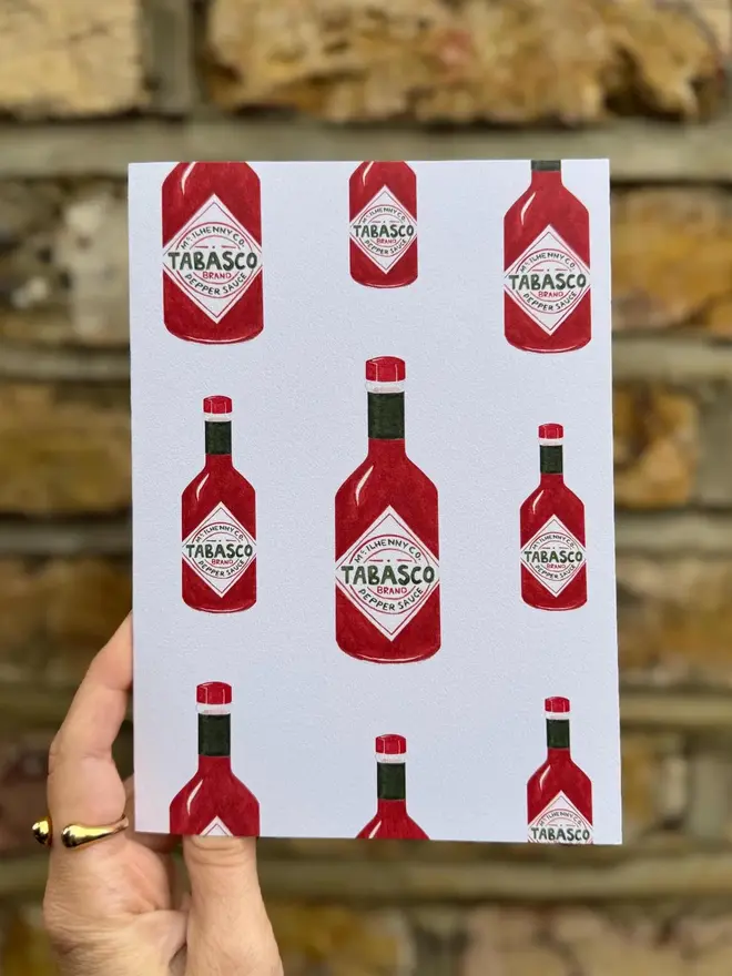 tabasco bottles illustrated card. card photographed against brick wall backdrop.