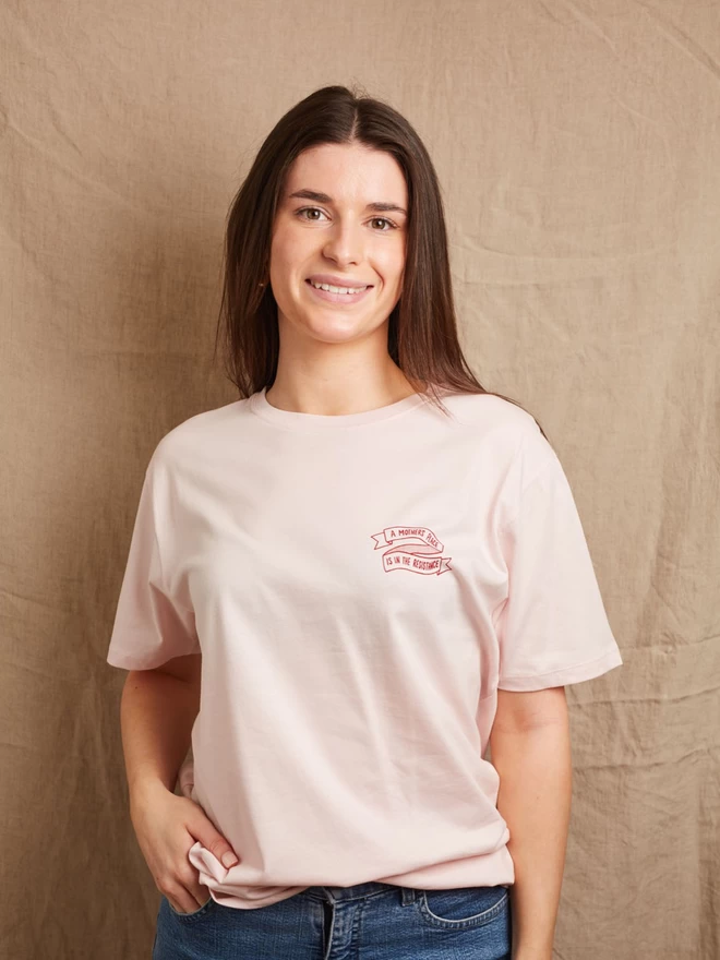 Model is showing the front of the Black & Beech pink A Mother’s Place is in the resistance t-shirt.