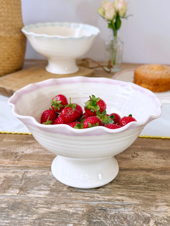 Undulating hand thrown porcelain stem bowls with satin cream glaze and pink or turquoise rim on a rustic table top