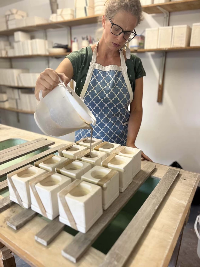 In her studio Katie is filling plaster egg cup moulds with slip (liquid clay) from a large plastic jug.