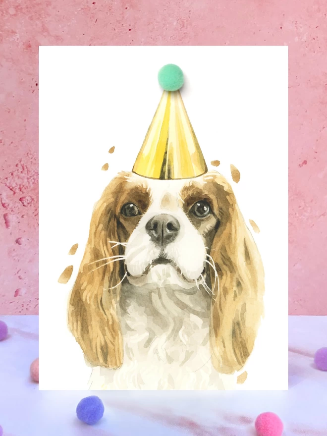 Cavalier King Charles Spaniel Pompom Birthday Card in front of a pink background and surrounded by pompoms