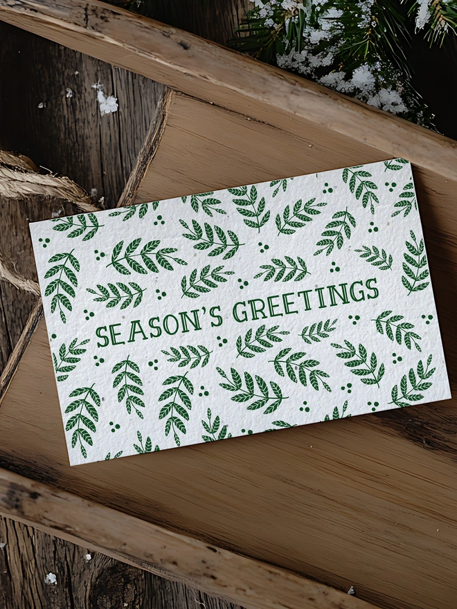Christmas card with 'Seasons Greetings' on it surrounded by green leaves. The card is in a Christmas scene
