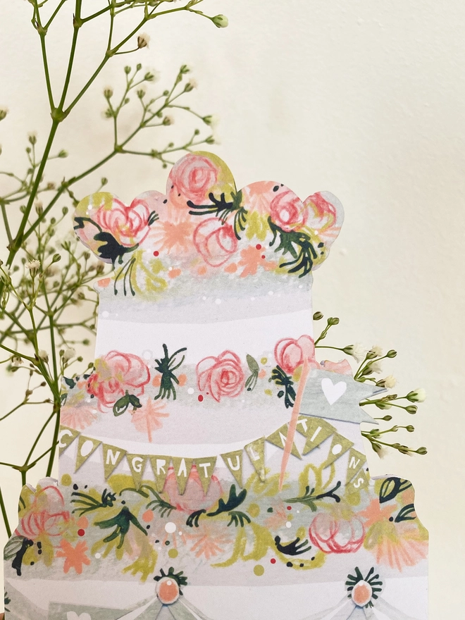 Esther kent illustrated greetings card in the shape of a tierd cake decorated with pink flowers and greenery.