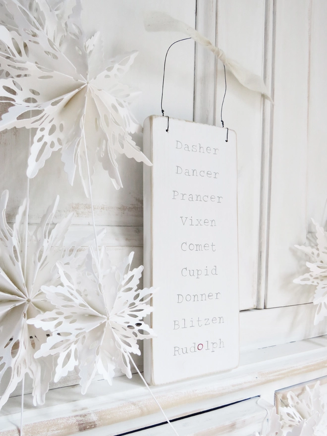 white painted wooden sign with reindeer names strung with wire and decorated with ribbon
