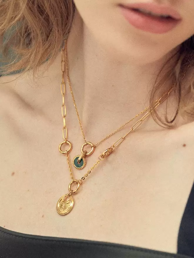 Woman wearing two gold necklaces styled with a malachite disc and a pancake lock pendant