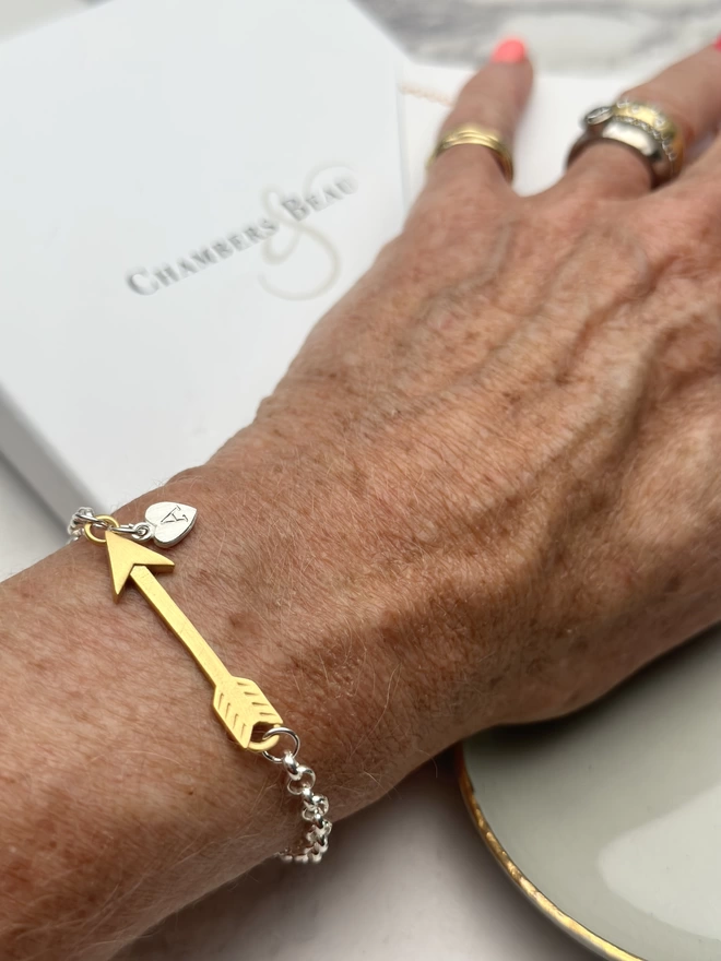 model wears sterling silver bracelet with gold arrow charm and small personalised silver heart charm