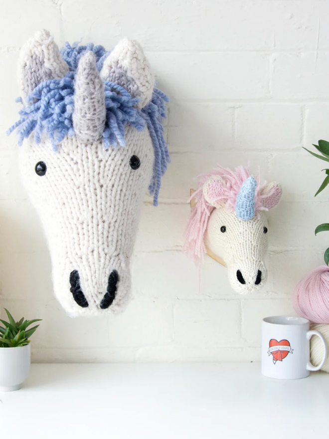 Unicorn Head Knitting Kit. A giant unicorn head in cream and blue next to a mini head in cream and pink.