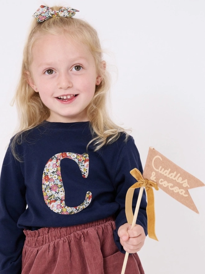 a 3 year old girl wearing a personalised kids personalised navy t-shirt with an initial cut from Libby liberty floral print on the front