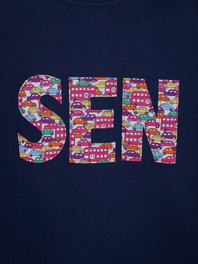 a personalised navy birthday t-shirt with a name cut from liberty cars and London buses print on the front