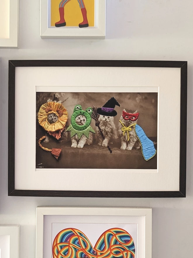 4 cats print in embroidered fancy dress hung in frame on wall 