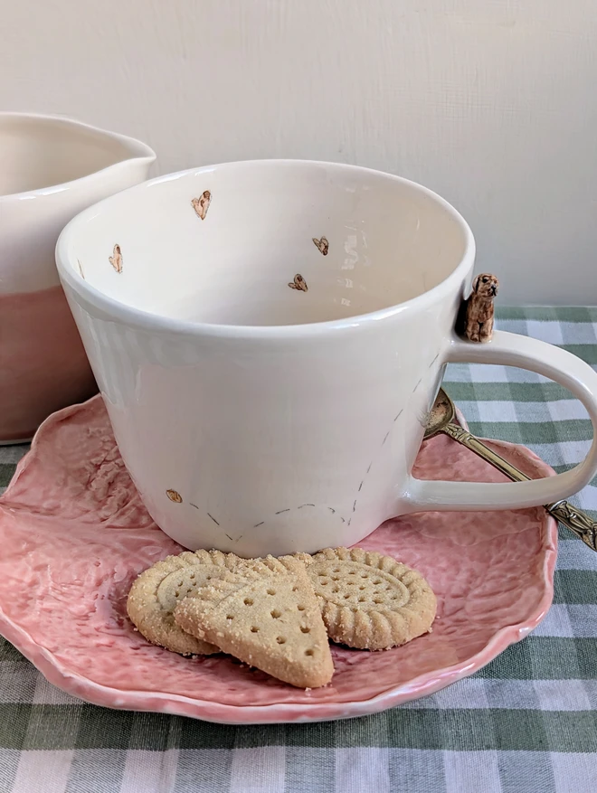 Brown Labrador sculpture on the handle of an off white ceramic cup with tiny pawprints and hearts inside the mug