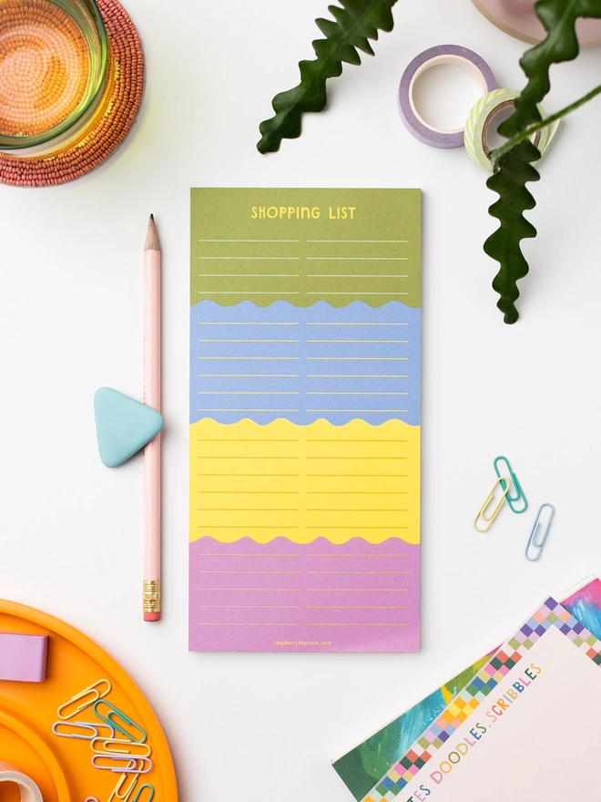 Raspberry Blossom shopping list pad sits on a desk among other colourful stationery items from the Raspberry Blossom ‘Happiness’ Stationery Collection