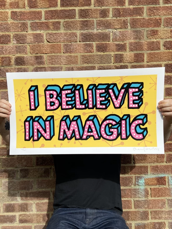 "I Believe In Magic" Hand Pulled Screen Print rectangular 1950s pattern background in deep yellow with the words i believe in magic printed on top in hand drawn lettering pink writing black outline 