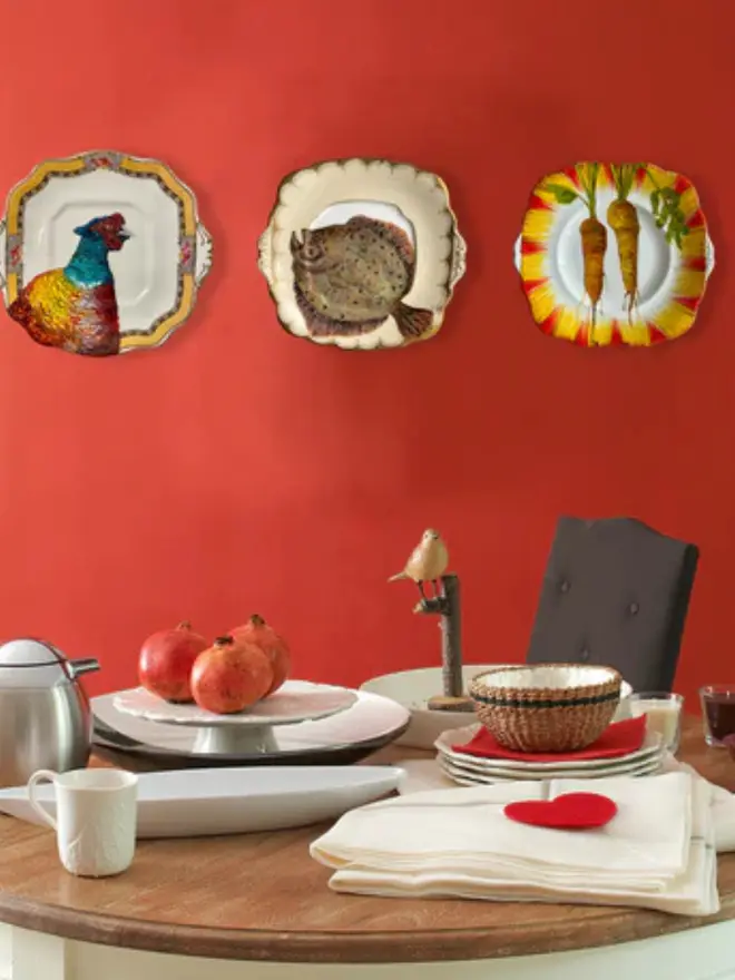 plate-scape. Oil Painted pheasant on a vintage cake plate, hanging on a red wall, behind a set table. 
