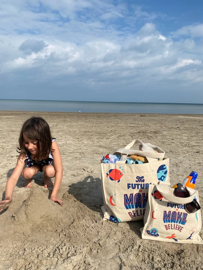 Bright graphic beach bags on the sand next to playing girl