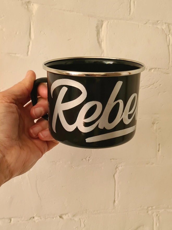 'Rebel' Enamel Mug, a colourful mug sitting on a white surface. held 