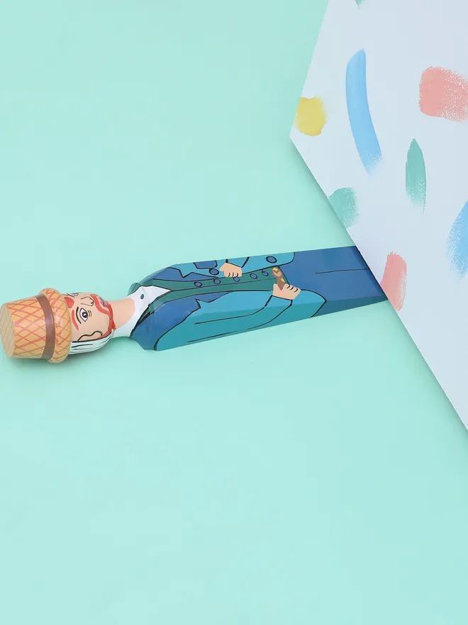 Wooden Door Stopper (Vinnie), a colourful wooden door stop sitting under a door.