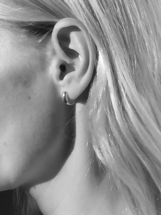 Black and white image of a model wearing a chunky silver ear huggie earring