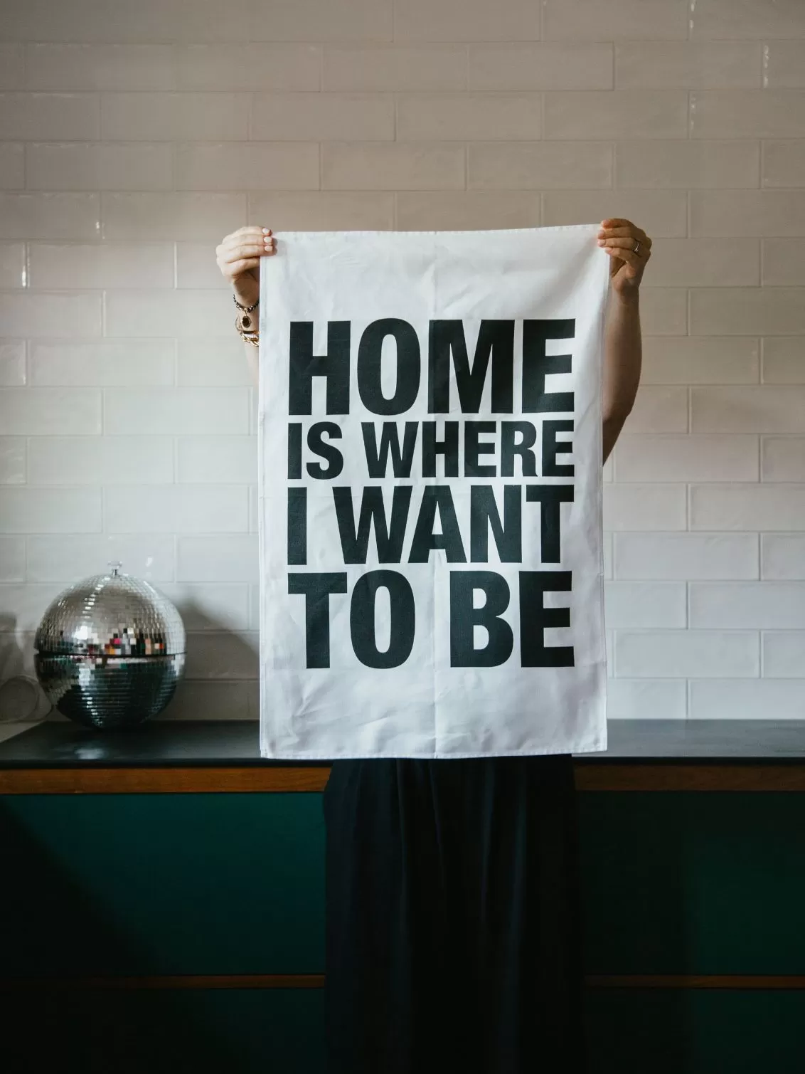 London Drying Home Is Where I Want To Be Tea Towel seen being held up in a kitchen.