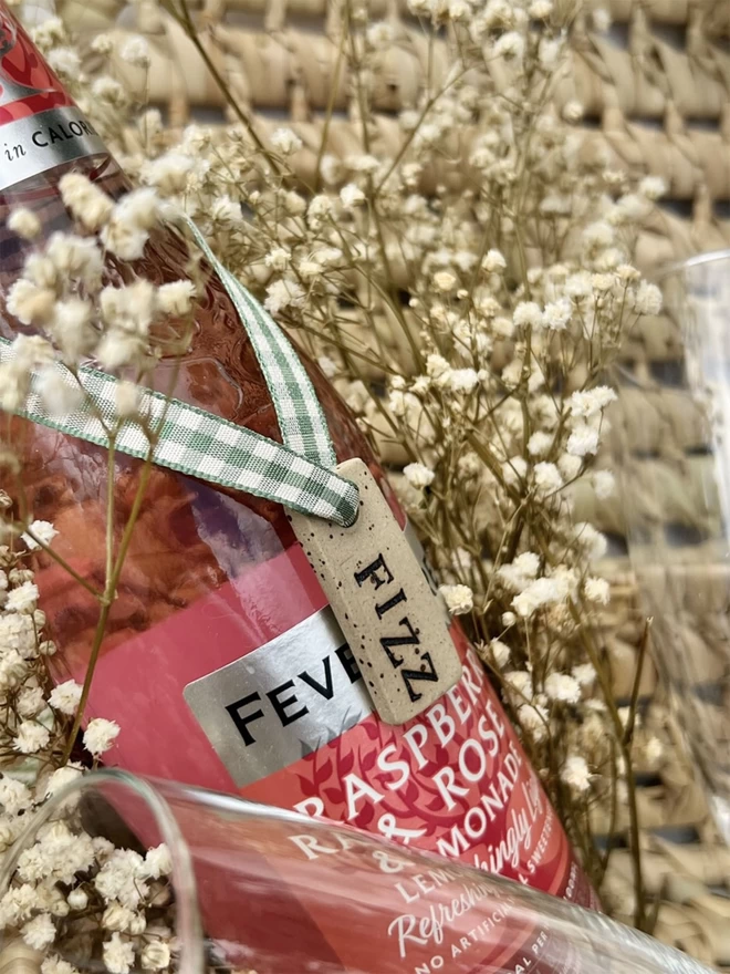 Bottle of pink lemonade with a ceramic tag embossed with the word 'Fizz' tied around it's neck with green gingham ribbon