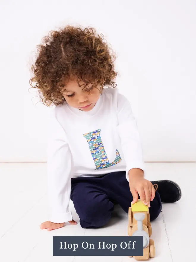 a 3 year old boy wearing a personalised kids white t-shirt with an initial cut from liberty cars and bus on the front