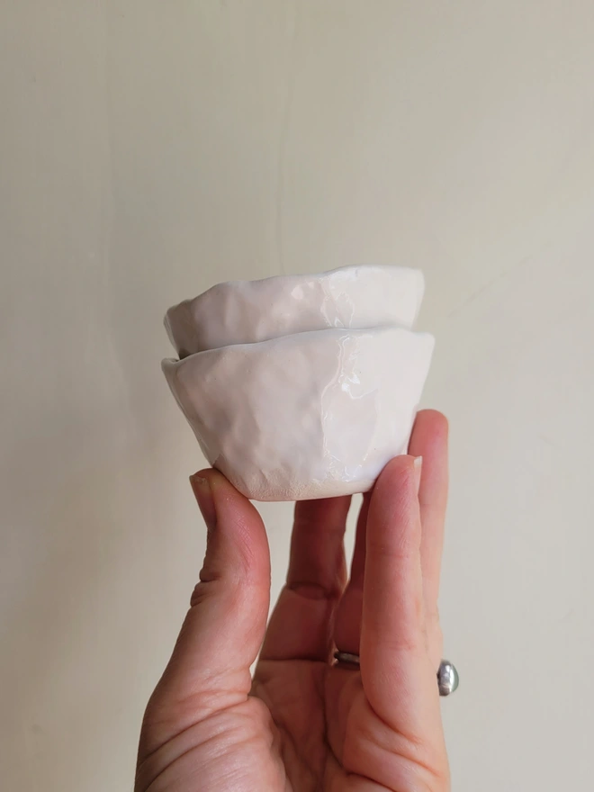 two white ceramic pinch pots held aloft in a hand
