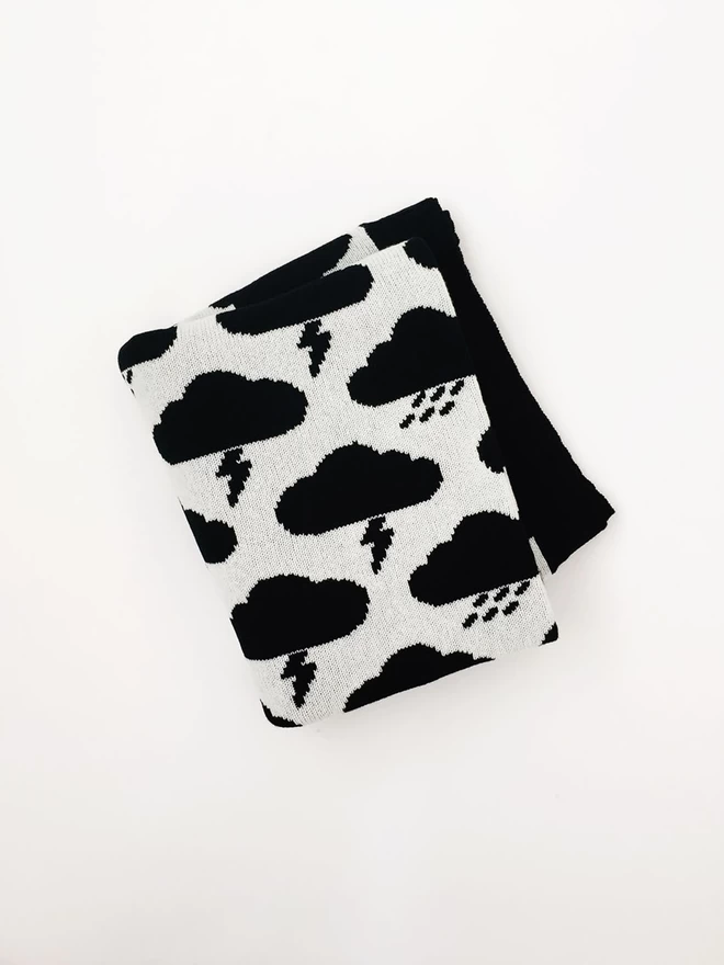 A folded junior blanket, photographed from above, showing a black and white storm cloud pattern and a glimpse of black trim.