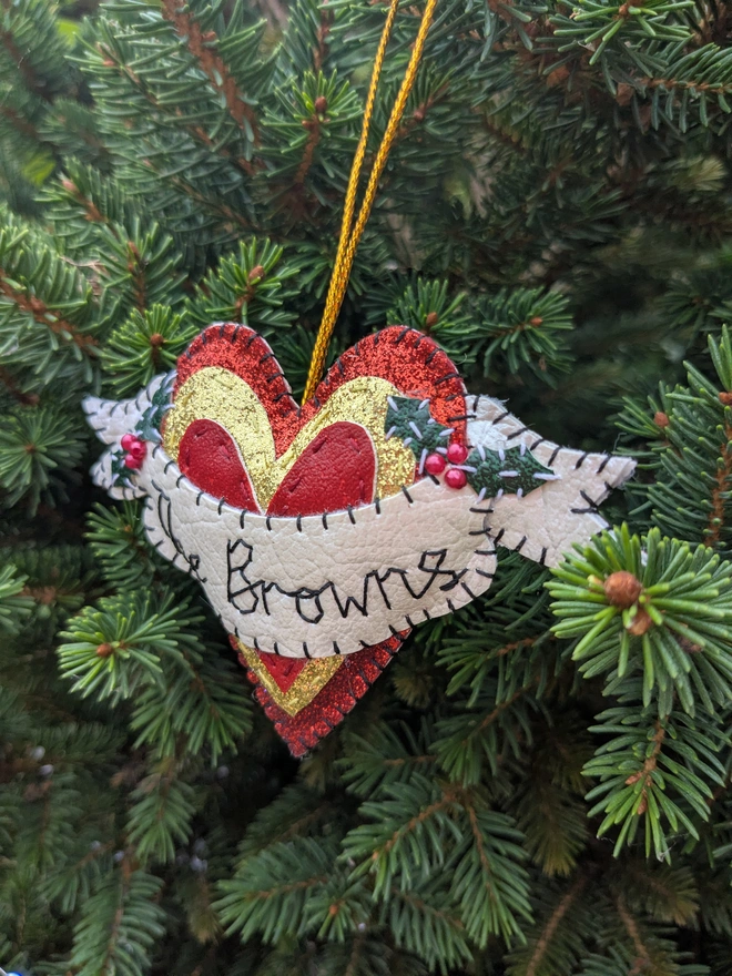 Hand stitched personalised heart Christmas decoration made from vegan-friendly faux leather, featuring a cream name banner, sparkly holly leaves, red berries and a gold hanging cord.