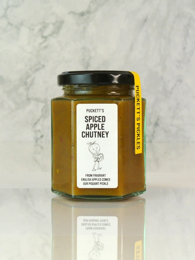spiced apple chutney. a jar of chutney photographed against a marble background. 